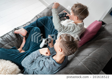 School aged boys sitting on sofa with game joysticks, side view from above. Children play videogames. Friends lifestyle. 101616522