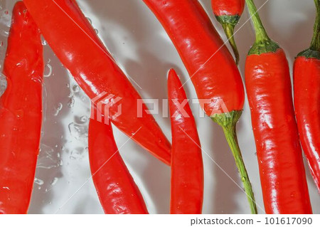Close-up of fresh slices chilli peppers on white background. Red chilli peppers in sparkling water on white background, close-up. Horizontal image 101617090