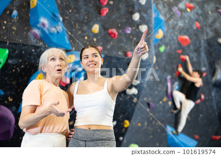 Young female climbing instructor explaining wall climbing to mature woman 101619574