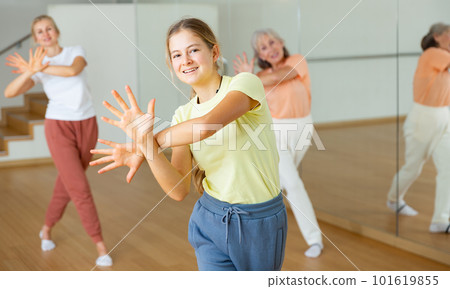 Teen girl with family doing aerobics exercises with group of people in dance center 101619855