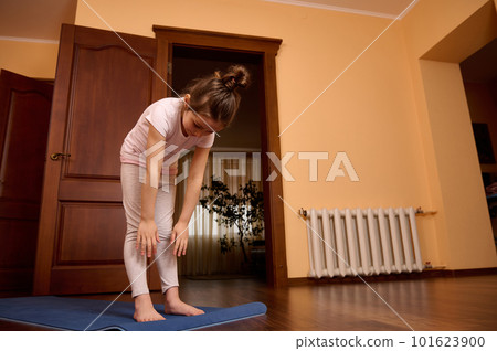 Lovely little child girl exercising, working out, practicing yoga, standing on a blue fitness mat in cozy home interior. Childhood. Healthy habits and active lifestyle concept. Sport. Fitness concept Lovely little child girl exercising, working out, practicing yoga, standing on a blue fitness mat in cozy home interior. Childhood. Healthy habits and active lifestyle concept. Sport. Fitness concept 101623900