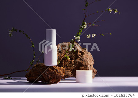 Front view of set of luxury cosmetic products on purple background. Brown stone with white flower as a highlight. 101625764