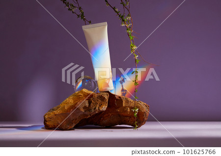 White plastic tube with facial moisturizer cream or facial cleanser on brown stone. Rainbow from sparkling crystal ball as highlight. White plastic tube with facial moisturizer cream or facial cleanser on brown stone. Rainbow from sparkling crystal ball as highlight. 101625766