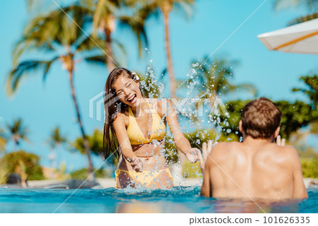 Happy swimming pool couple having fun laughing splashing water on luxury resort hotel travel holiday together on summer vacation. Asian woman, caucasian man in love on honeymoon 101626335