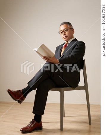 Senior man sitting on a chair and reading 101627558