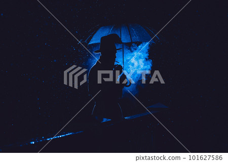 male detective in a hat and raincoat under an umbrella smokes at night male detective in a hat and raincoat under an umbrella smokes at night 101627586