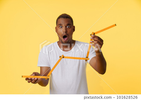 Concept of income growth, amazed African American man holding folding ruler and showing growth chart on the stock exchange. Man is standing on bright yellow background with copy space for designers to Concept of income growth, amazed African American man holding folding ruler and showing growth chart on the stock exchange. Man is standing on bright yellow background with copy space for designers to 101628526