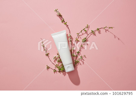 White empty plastic tube with facial moisturizer cream or facial cleanser and small branches flower on pink background. Mockup for presentation of cosmetic products. Top view, flat lay. 101629795