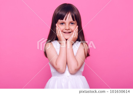 Cute pleasant looking small girl wearing stylish white dress looking at camera with charming happy expression, being satisfied, admiring something, isolated over pink background. Cute pleasant looking small girl wearing stylish white dress looking at camera with charming happy expression, being satisfied, admiring something, isolated over pink background. 101630614