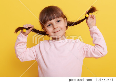 Caucasian little girl pulling herself in pigtails while looking directly at camera with cute charming smile, kid in casual pale pink shirt isolated over yellow background. Caucasian little girl pulling herself in pigtails while looking directly at camera with cute charming smile, kid in casual pale pink shirt isolated over yellow background. 101630671