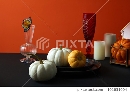 Front view of pumpkins, candles, wine glasses and plates on table on red background. Halloween setting table for dinner, trick or treat. 101631004