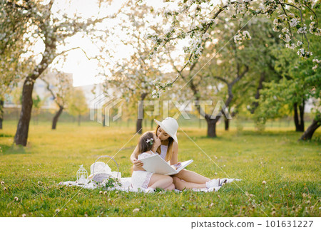 Mom and little daughter are looking at a family album with photos in the summer in the garden. Mom kisses her daughter. Family values 101631227