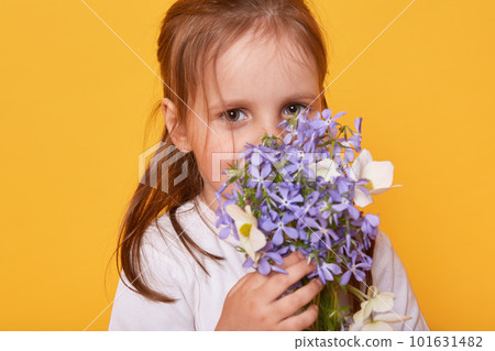 Studio shot of cute little girl wearing white shirt smelling bouquet of flower, present for her mummy, toddler wants to congratulet her mommy, standing against yellow sudio wall. Happy Mother's Day! Studio shot of cute little girl wearing white shirt smelling bouquet of flower, present for her mummy, toddler wants to congratulet her mommy, standing against yellow sudio wall. Happy Mother's Day! 101631482