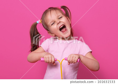 Adorable girl holds skipping rope in hands. Charmig female child with opened mouth and narrowed eyes with happy expression. LIttle cute model poses in photo studio isolated over pink bckground. Adorable girl holds skipping rope in hands. Charmig female child with opened mouth and narrowed eyes with happy expression. LIttle cute model poses in photo studio isolated over pink bckground. 101631533