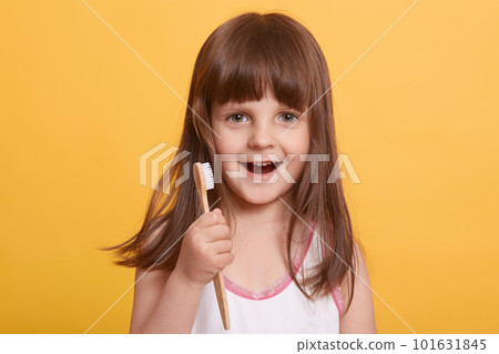 Studio shot of beautiful happy surprised dark haired little girl in bathroom, brushing teeth with excited facial expression, posing isolated over yellow background. Childhood, daily procedures concept 101631845