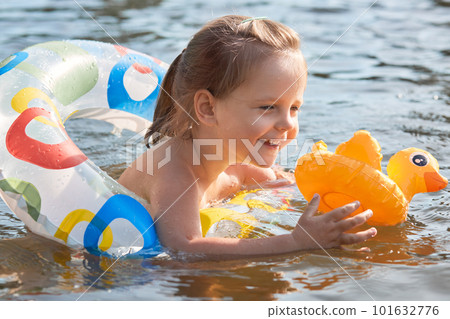 Outdoor shot of liitl girl in lifebuoy, happy child swims in pond, todler in rubber ring having fun in river, holds yellow duck, child has happy facial expression, spends time in open air with parents Outdoor shot of liitl girl in lifebuoy, happy child swims in pond, todler in rubber ring having fun in river, holds yellow duck, child has happy facial expression, spends time in open air with parents 101632776