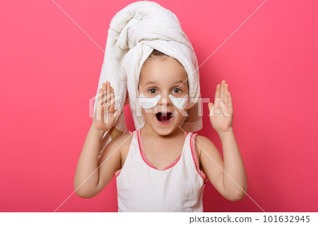 Close up portrait of beautiful excited little girl wearing white towel after shower. Studio shot isolated over pink background, female child with hands up and opened mouth, expresses astonishment. 101632945