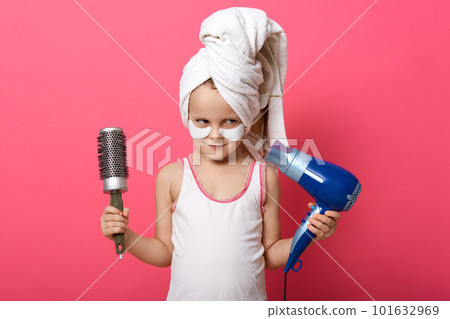 Indoor shot of beautiful cute girl with hair dryer and comb in both hands, lady with white towel on head and putches under eyes, posing isolated over pink background. Children fashion concept. Indoor shot of beautiful cute girl with hair dryer and comb in both hands, lady with white towel on head and putches under eyes, posing isolated over pink background. Children fashion concept. 101632969