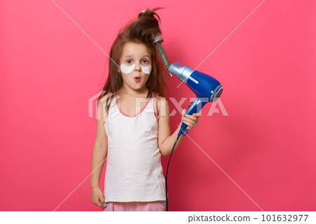 Portrait of pretty little girl with tangled hair comb in her hair, kid holding hair dryer and having astonished facial expression, has problem, model posing isolated on pink background. Kid's fashion. Portrait of pretty little girl with tangled hair comb in her hair, kid holding hair dryer and having astonished facial expression, has problem, model posing isolated on pink background. Kid's fashion. 101632977