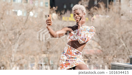 Trendy black queer person in dress taking selfie on street 101634415