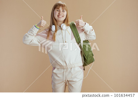 Portrait of happy girl in beige tracksuit showing thumbs up 101634457