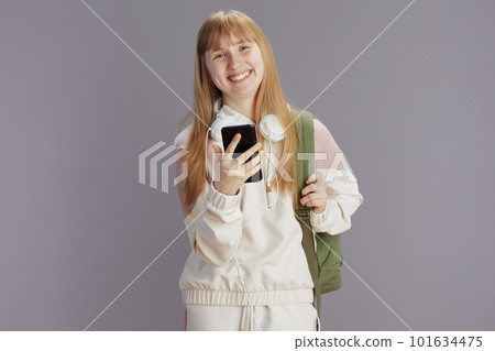 smiling teenage girl in beige tracksuit using phone 101634475