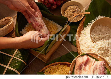 Hands putting fatty pork in box lined with dong leaves when making sticky rice cake (Chung cake). Traditional lunar new year food. concept for advertising Hands putting fatty pork in box lined with dong leaves when making sticky rice cake (Chung cake). Traditional lunar new year food. concept for advertising 101634594