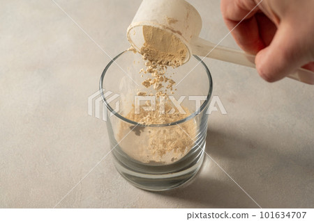 Pouring protein powder from scoop, in glass a glass. Making protein drink. Pouring protein powder from scoop, in glass a glass. Making protein drink. 101634707