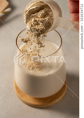 Pouring protein powder from scoop, in glass with milkshake. 101634712