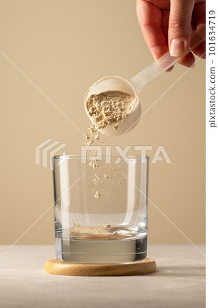 Pouring protein powder from scoop, in glass a glass. Making protein drink. 101634719