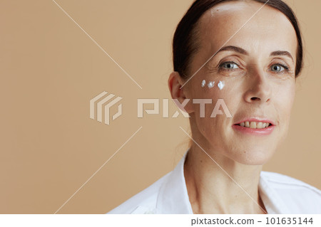 modern woman with eye cream on face on beige background 101635144