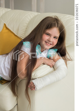 Child with a cast on a broken wrist or arm sits on a couch. Recovery and kid concept. 101636071