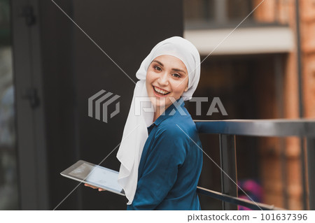 Smiling muslim girl using digital tablet, browsing Internet or social networks outdoor 101637396