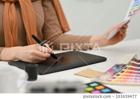 Young creative woman using graphic tablet and working with color swatch samples at modern workplace 101639477