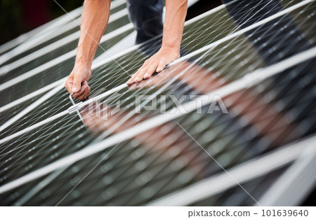 Man technician mounting photovoltaic solar moduls on roof of house. Close up of engineer installing solar panel system outdoors with help of hex key. Concept of alternative and renewable energy. Man technician mounting photovoltaic solar moduls on roof of house. Close up of engineer installing solar panel system outdoors with help of hex key. Concept of alternative and renewable energy. 101639640