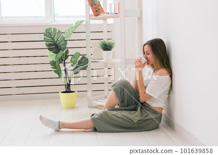 Dreaming girl sitting on floor at home and drink tea from cup 101639858