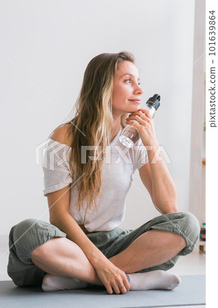Positive girl sitting on fitness mat resting after pilates or yoga practice. Mindfulness and wellbeing concept. Positive girl sitting on fitness mat resting after pilates or yoga practice. Mindfulness and wellbeing concept. 101639864