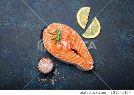 Fresh raw salmon fillet steak with rosemary on dark blue rustic stone background with rose salt and lemon top view, healthy balanced diet and nutrition Fresh raw salmon fillet steak with rosemary on dark blue rustic stone background with rose salt and lemon top view, healthy balanced diet and nutrition 101641304
