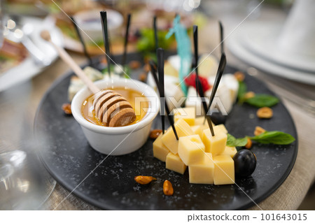 a dish of various delicious cheeses and a plate of honey. a dish of various delicious cheeses and a plate of honey. 101643015