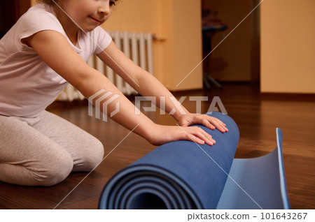 Details on hands of a 5-6 years Caucasian determined child girl in sportswear, folding blue rubber gym mat after yoga practice or workout indoors. Sport. Fitness. Active and healthy lifestyle concept Details on hands of a 5-6 years Caucasian determined child girl in sportswear, folding blue rubber gym mat after yoga practice or workout indoors. Sport. Fitness. Active and healthy lifestyle concept 101643267