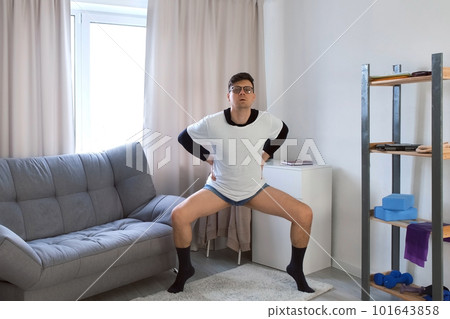 Nerd funny man in glasses doing fitness exercises squats and plie at home. Nerd funny man in glasses doing fitness exercises squats and plie at home. 101643858