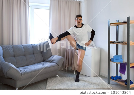 Funny nerd man is doing balancing yoga pose at home lifting leg in side. Funny nerd man is doing balancing yoga pose at home lifting leg in side. 101643864