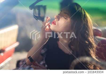 successful business lady driving a car in sunglasses paints her lips with lipstick while looking in the mirror. 101643934