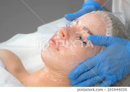 Cosmetologist doctor applies film on cream with anesthesia on woman's face. Cosmetologist doctor applies film on cream with anesthesia on woman's face. 101644038