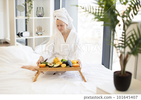Lady putting tray table with fruits and cosmetics on bed Lady putting tray table with fruits and cosmetics on bed 101645407