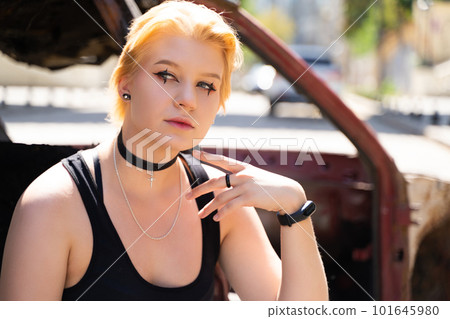 glamorous girl in pants and short hair and makeup posing near a broken old car. 101645980