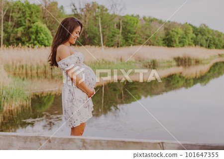 Portrait of pregnant woman holding big belly baby bump happy and smilling of happiness in 3rd trimester in forest by lake. Asian expectant mother holding tummy. Healthy pregnancy concept. 101647355