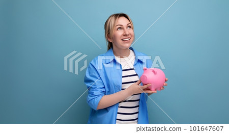 blond smiling girl in casual outfit holding a piggy bank on a blue background with copy space blond smiling girl in casual outfit holding a piggy bank on a blue background with copy space 101647607