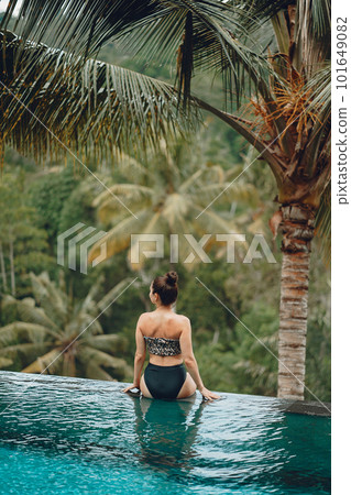 Woman sititng by the swimming pool. Lady in a swimsuit. Girl relaxing by the pool at a beach club in Bali Indonesia 101649082