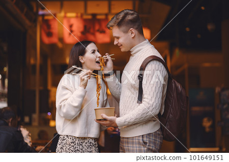 newlywed couple eating noodles with chopsticks in Shanghai outside a food market near Yuyuan. Couple eating authentic local food. husband and wife eating chinese food outisde of a food hall 101649151